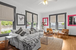 Un salon moderne avec un canapé, des fauteuils, une table basse et une grande fenêtre équipée de stores.