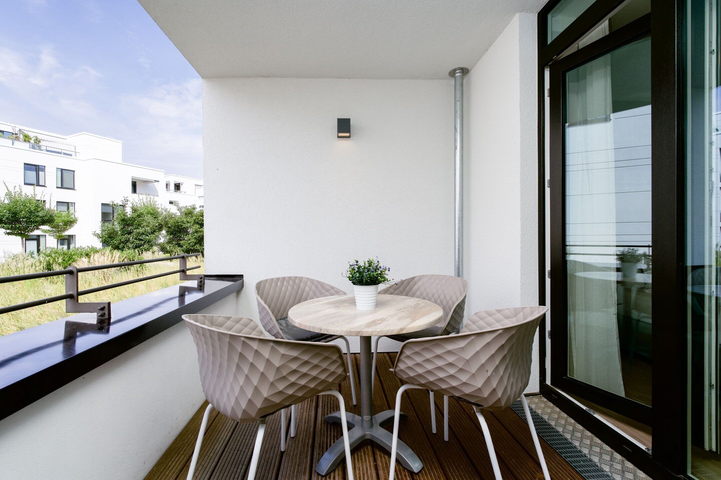 Un balcón con mesa y sillas, una planta en maceta y vistas a edificios.