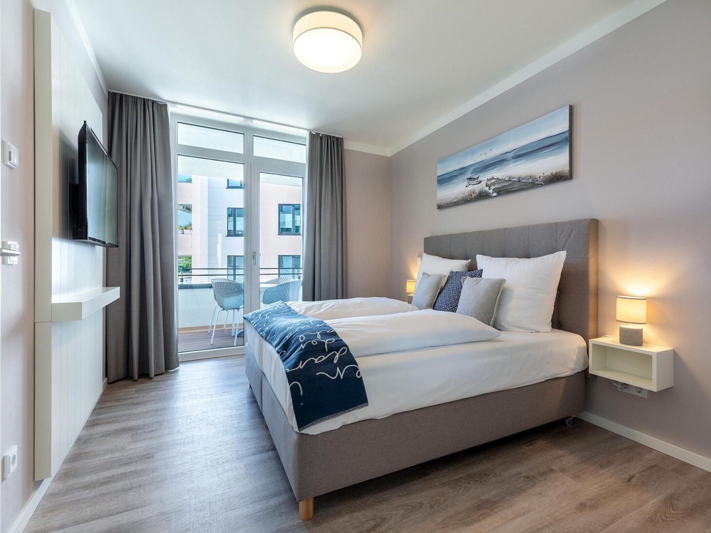 Quarto de hotel moderno com uma cama grande, televisão, varanda e um quadro na parede.