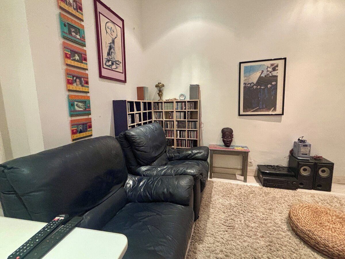 Un soggiorno con un divano in pelle nera, una libreria, un quadro incorniciato e un tavolino con una scultura a busto.