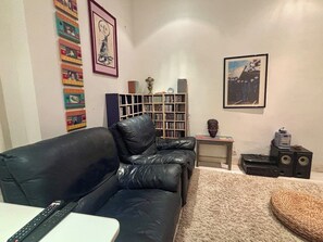 Ein Wohnzimmer mit einem schwarzen Ledersofa, einem Bücherregal, einem gerahmten Bild und einem kleinen Tisch mit einer Büsten-Skulptur.