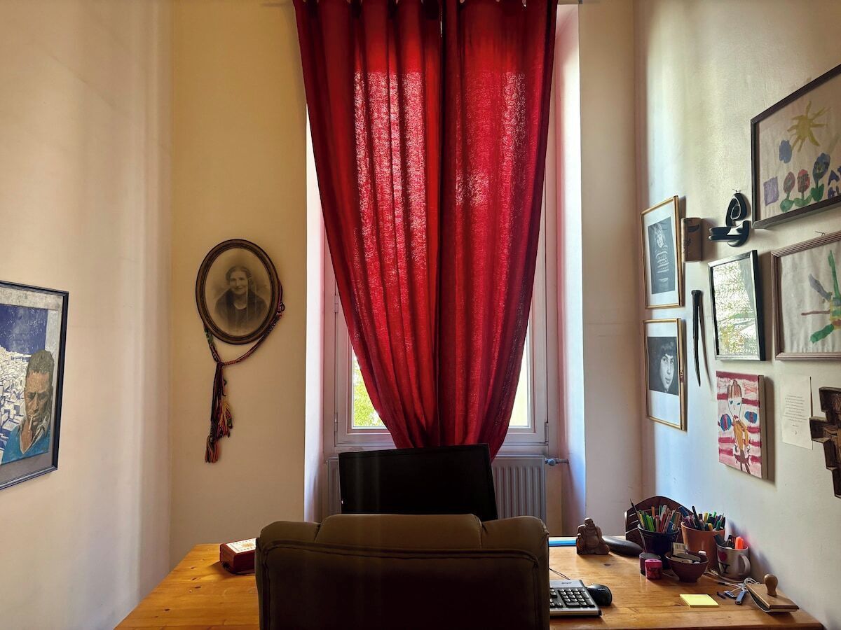 Une pièce comprenant un bureau, une chaise, une fenêtre avec des rideaux rouges et divers tableaux encadrés accrochés aux murs.