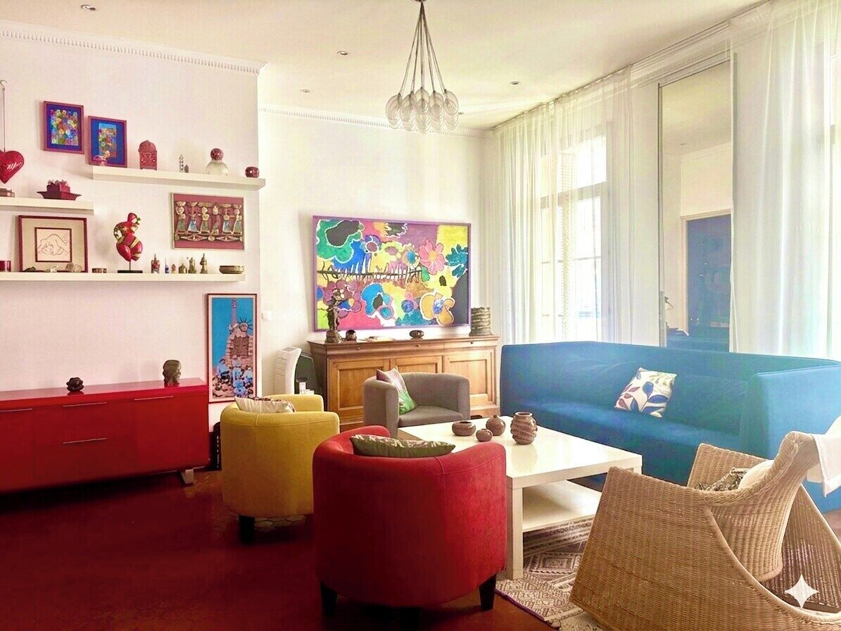 Un salon avec un canapé bleu, des fauteuils rouges et jaunes, une table basse blanche et un tableau abstrait aux couleurs vives accroché au mur.