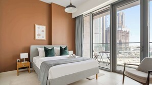 A modern bedroom with a large bed, a bedside table, a chair, and a view of the cityscape through large windows. - Silkhaus Chic Canalside 3BR in Al Wasl Dubai (Dubai)