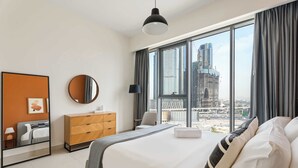 A modern hotel room with a large bed, a dresser, a mirror, and a view of a cityscape. - Silkhaus Chic Canalside 3BR in Al Wasl Dubai (Dubai)