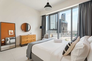 A modern hotel room with a large bed, a dresser, a mirror, and a view of a cityscape. - Silkhaus Chic Canalside 3BR in Al Wasl Dubai (Dubai)