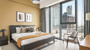 A modern bedroom with a large bed, two bedside tables, a chair, and a view of a cityscape through floor-to-ceiling windows. - Silkhaus Chic Canalside 3BR in Al Wasl Dubai (Dubai)
