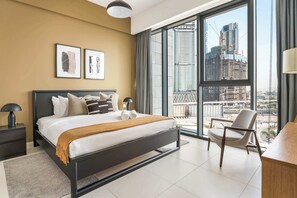 A modern bedroom with a large bed, two bedside tables, a chair, and a view of a cityscape through floor-to-ceiling windows. - Silkhaus Chic Canalside 3BR in Al Wasl Dubai (Dubai)