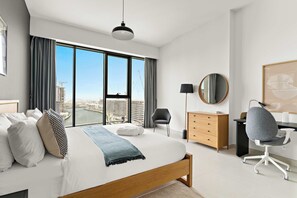 Ein modernes Hotelzimmer mit einem großen Bett, einem Schreibtisch, einem Stuhl, einer Kommode und Blick auf die Stadtlandschaft.
