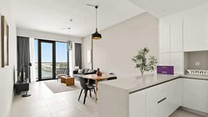 Eine moderne Küche mit weißen Schränken, ein Essbereich mit rundem Tisch und Stühlen sowie ein Blick auf die Stadt durch große Fenster.