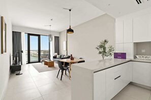 A modern kitchen with white cabinetry, a dining area with a round table and chairs, and a view of a cityscape through large windows. - Silkhaus Canal Side 2bdr Apartment in Al Wasl (Dubai)