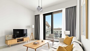 A modern hotel room with a flat-screen TV, a wooden coffee table, a sofa with cushions, a standing lamp, and a view of the city through large windows. - Silkhaus Scenic Waterfront 2BR in Al Wasl (Dubai)