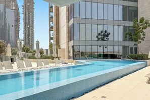 A modern building with a swimming pool, lounge chairs, and umbrellas. - Silkhaus Scenic Waterfront 2BR in Al Wasl (Dubai)