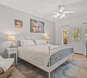 Ein Schlafzimmer mit einem Bett, Nachttischen, einem Deckenventilator und Kunstwerken an den Wänden.