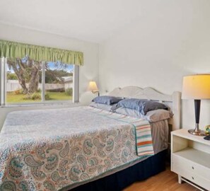 A bedroom with a bed, a bedside table with a lamp, a window with curtains, and a view of greenery outside. - 3BR Pool Home for 8 Easy Access to I-75 and I-4 (Valrico)