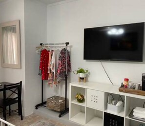 A room with a TV mounted on the wall, a clothing rack with various garments, a small plant on a shelf, and a desk with a chair. - 3BR Pool Home for 8 Easy Access to I-75 and I-4 (Valrico)
