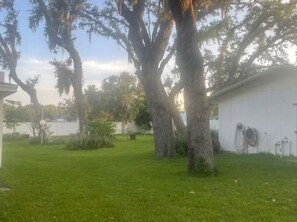 A residential area with a grassy lawn, trees, and a white building with a garage. - 3BR Pool Home for 8 Easy Access to I-75 and I-4 (Valrico)