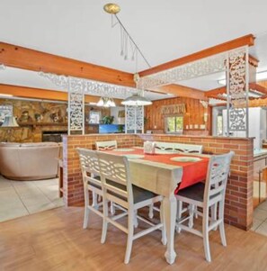 A dining area with a brick wall, wooden ceiling beams, and a table with chairs. - 3BR Pool Home for 8 Easy Access to I-75 and I-4 (Valrico)