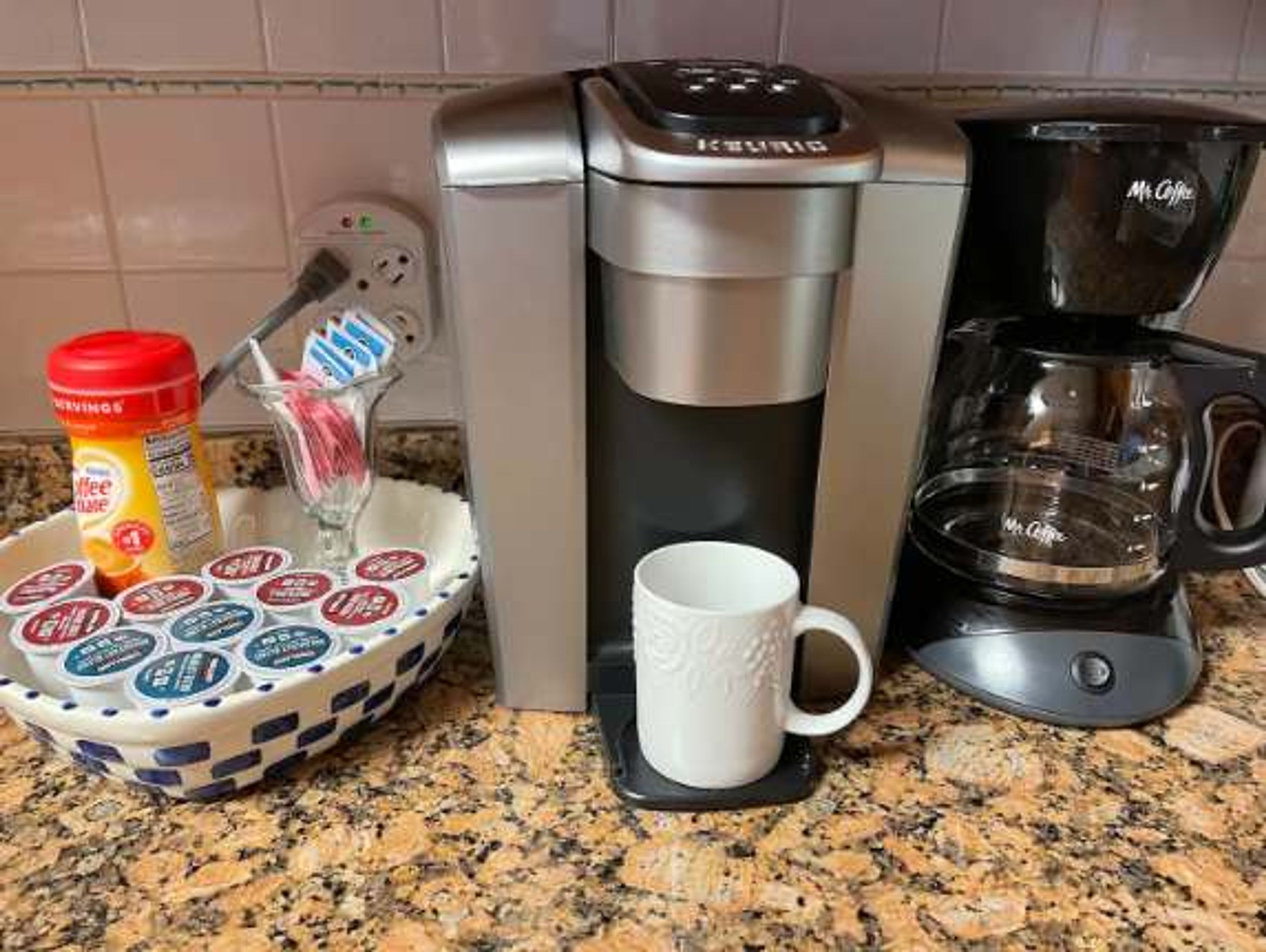 Eine Kaffeemaschine, eine Tasse und eine Schale mit Kaffeekapseln auf einer Arbeitsfläche.