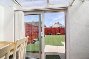 A glass door leading to a backyard with a red fence, a lawn, and a patio area. - 56 Steart Gardens (Burnham-on-Sea)