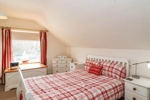A bedroom with a bed, a desk, a chair, a radio, and a window with curtains. - 56 Steart Gardens (Burnham-on-Sea)