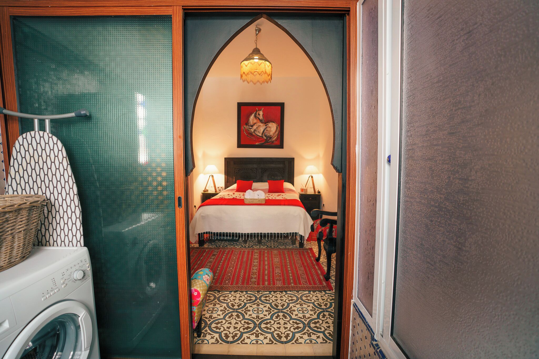 A compact hotel room with a bed, a washing machine, a small rug, and a decorative wall piece.