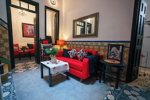 A cozy living room with a red sofa, a small table with a vase, and a mirror on the wall.