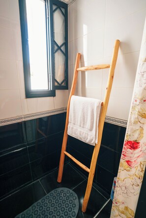 Een badkamer met een houten ladder, een witte handdoek en een douchegordijn met een patroon.