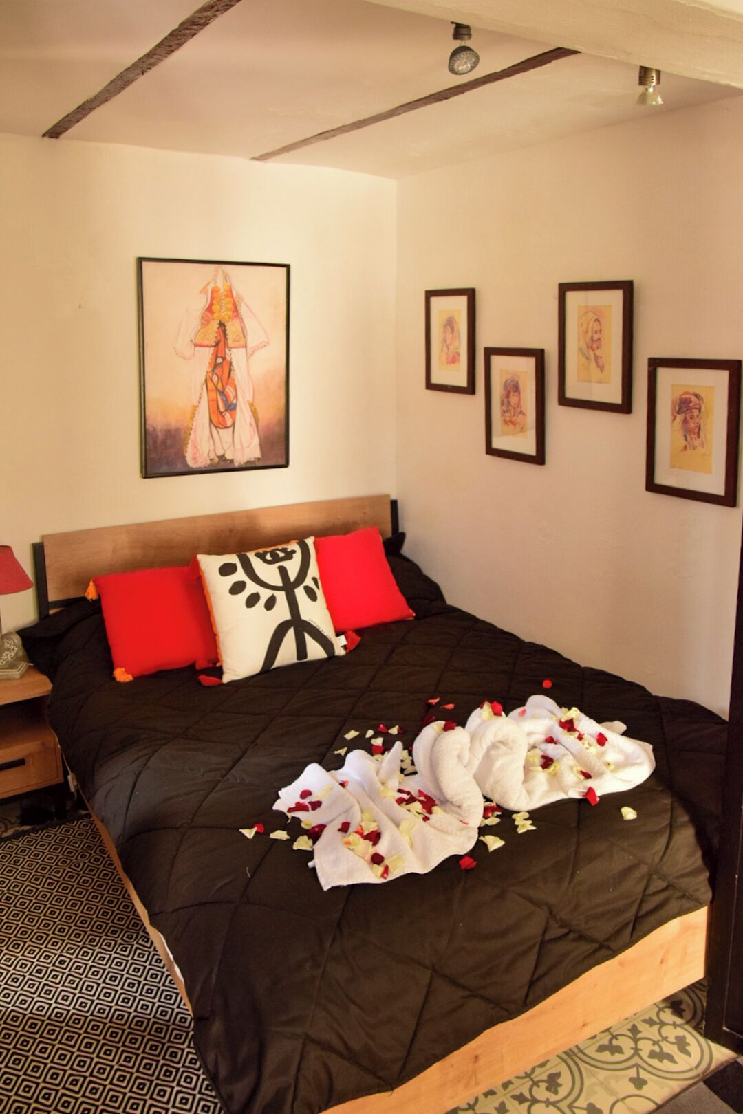 A bed with a black quilt, red and white pillows, and a wall with framed artwork.