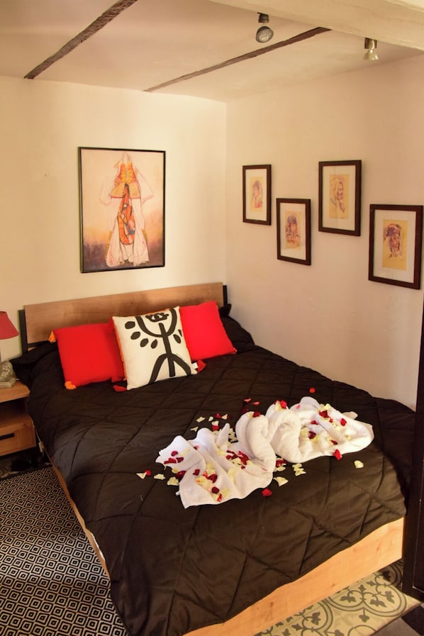 A bed with a black quilt, red and white pillows, and a wall with framed artwork.