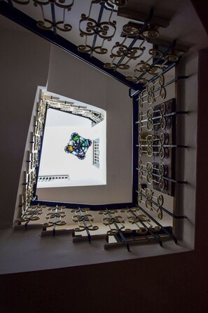 A room with a large window, a patterned metal railing, and a view of a building outside.