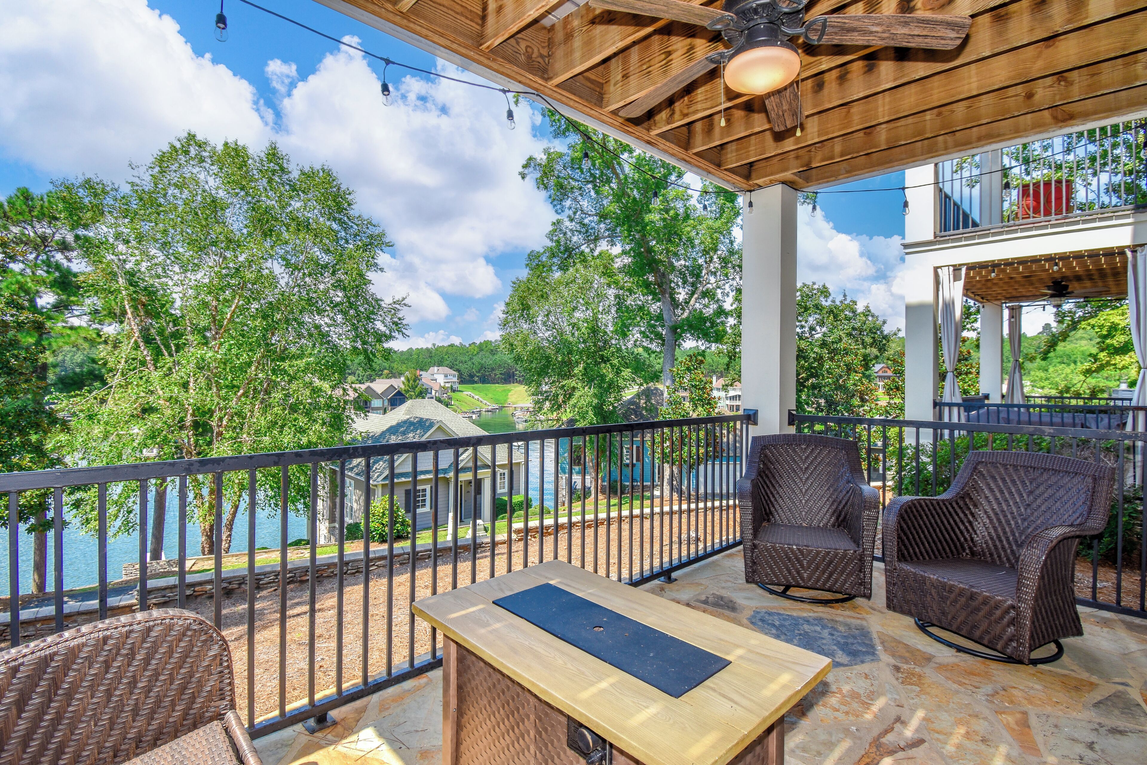 A covered outdoor area with wicker furniture, a table, and a view of a lake and buildings in the distance.