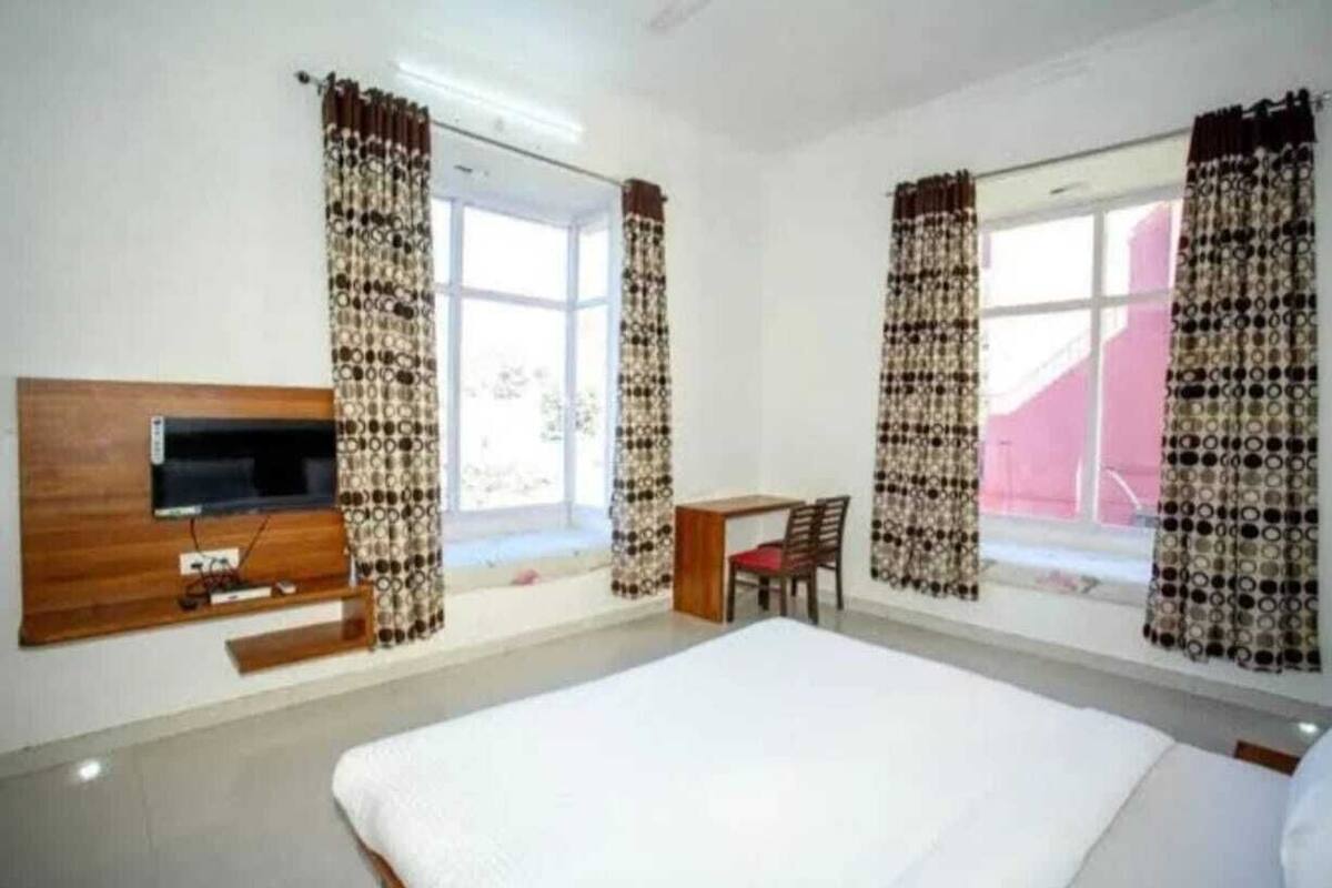 A room with a bed, a TV mounted on the wall, a desk with a chair, and patterned curtains.