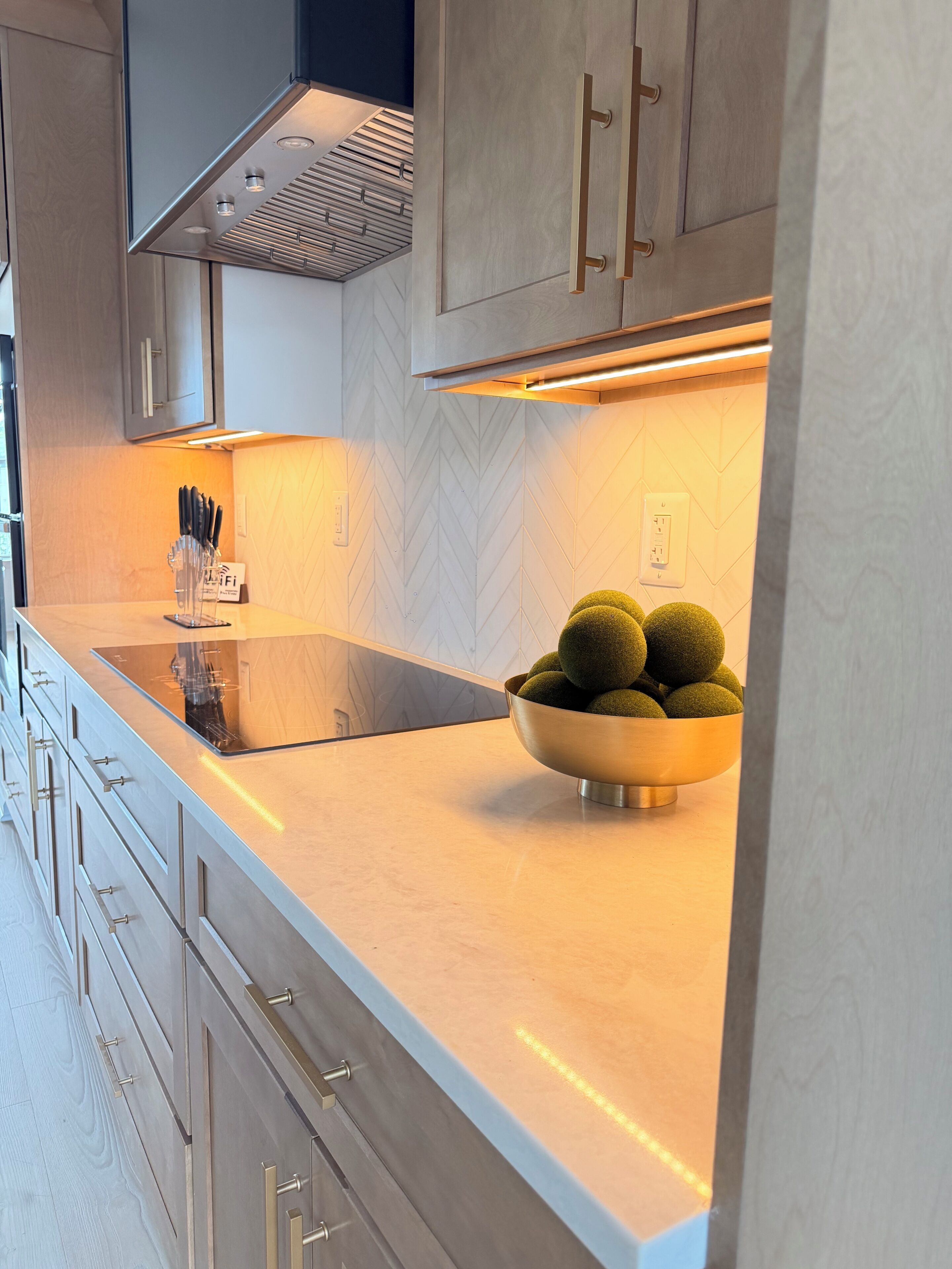 A modern kitchen with a stainless steel countertop, a bowl of green spherical objects, and a built-in oven.