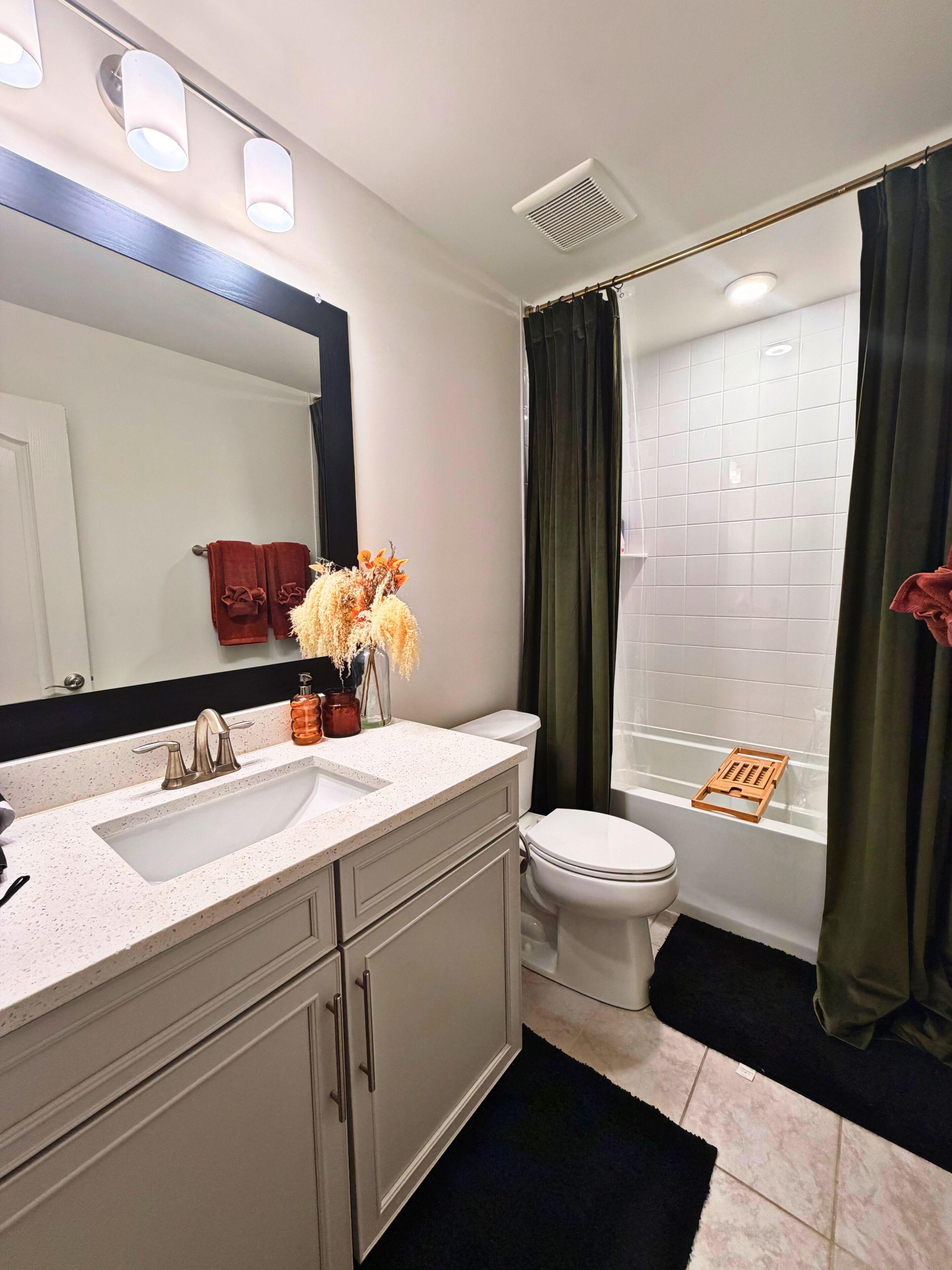Une salle de bain avec un lavabo blanc, deux robinets, un miroir, des toilettes et une douche avec des rideaux verts.