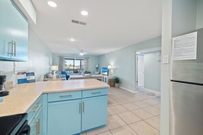 A kitchen with blue cabinets, a stainless steel refrigerator, and a dining area with a view. - Lei Lani Mini Tower 117N by Liquid Life (Orange Beach)
