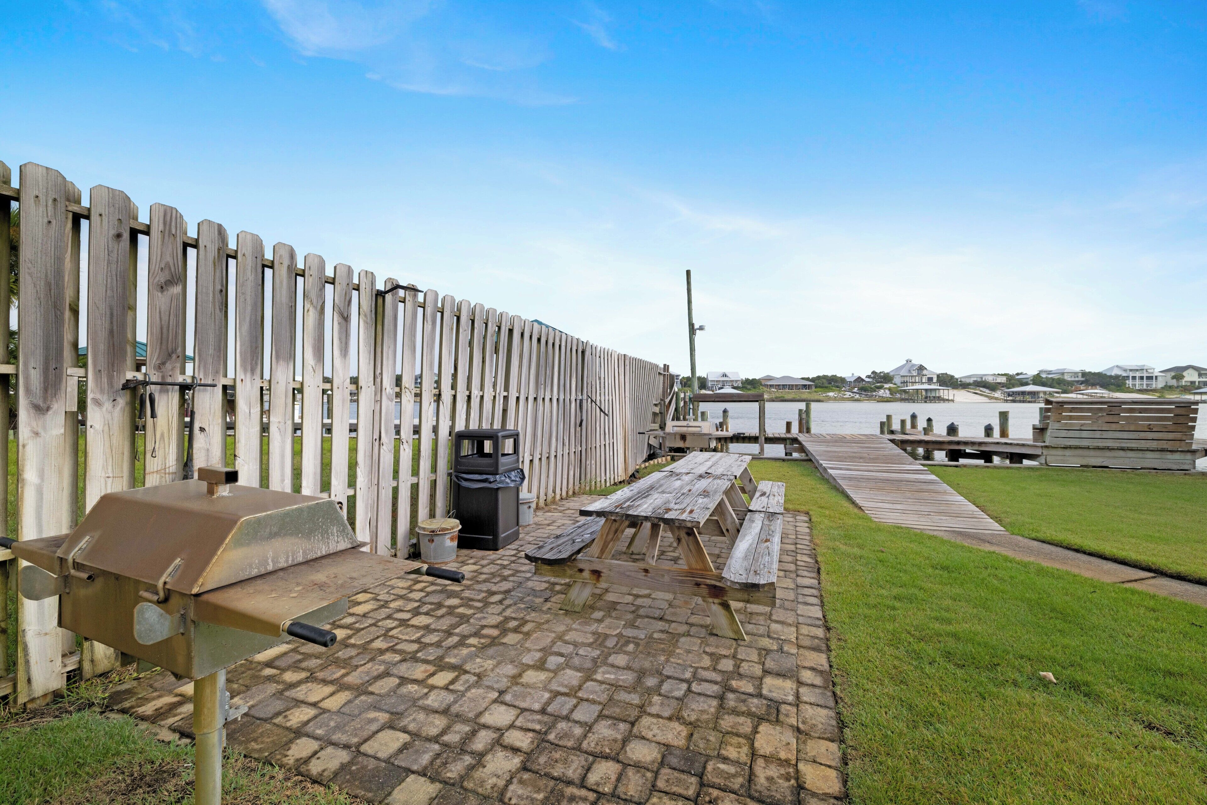 A patio with a grill, picnic table, and trash can.