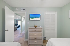 Ein Schlafzimmer mit einem Bett, einem Schminktisch, einem Fernseher an der Wand und einem Kleiderschrank.