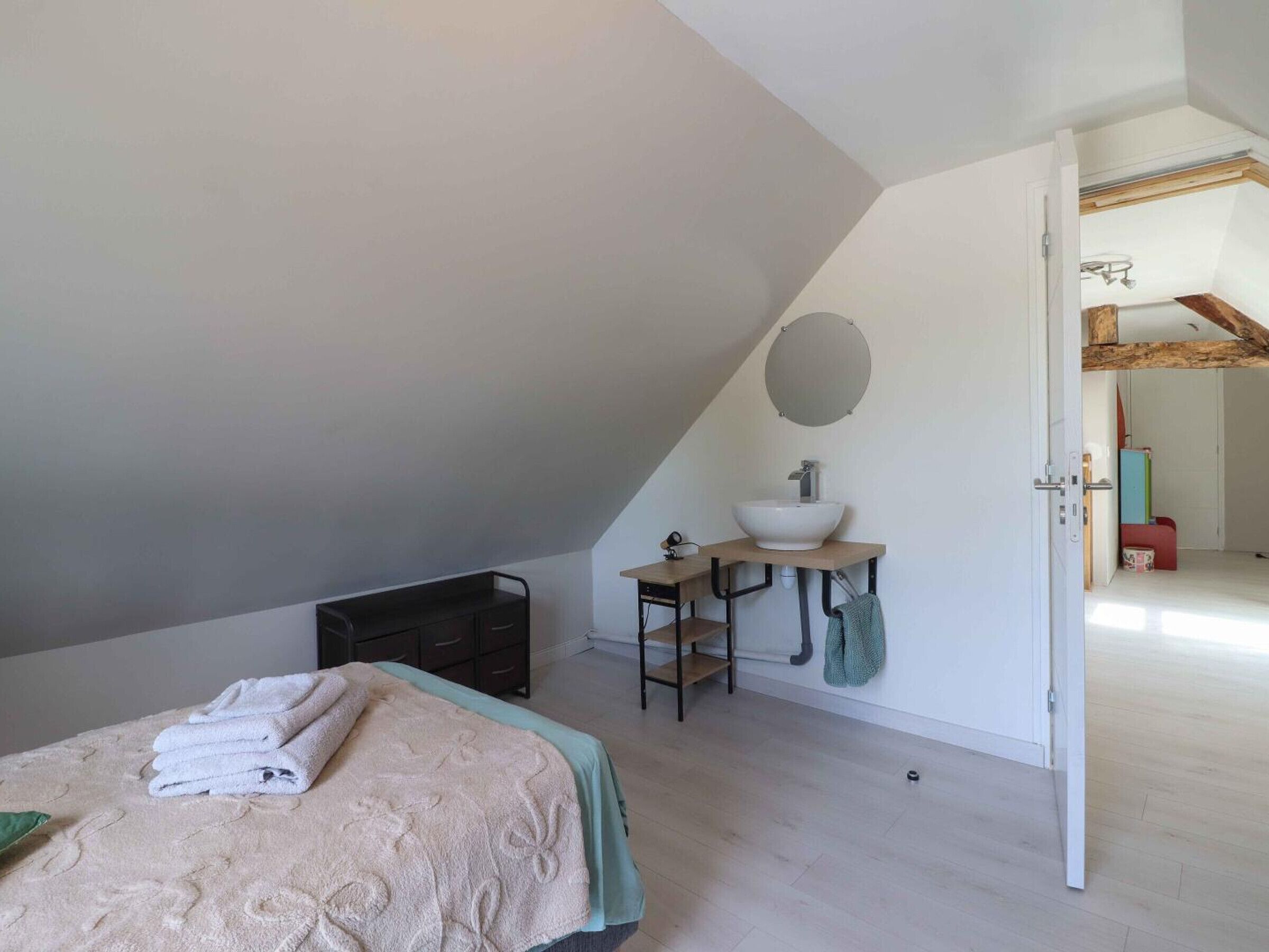 A bedroom with a bed, a bedside table, a built-in bench, a wall-mounted mirror, and a door leading to another room.