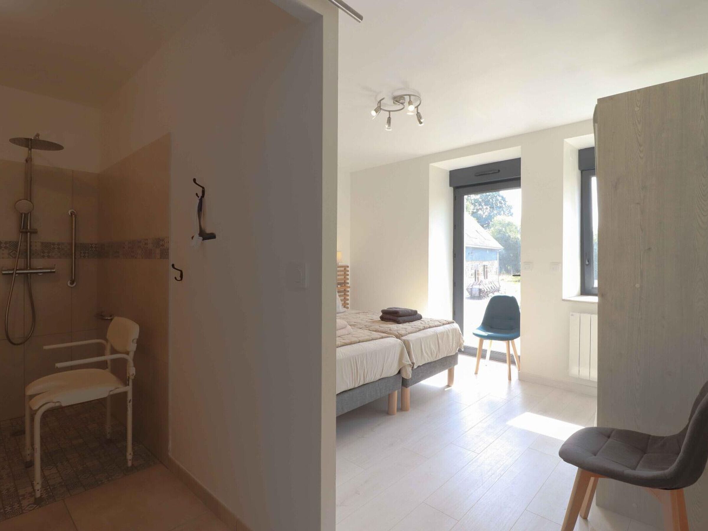 Habitación con ducha, silla de ruedas, cama y una silla.