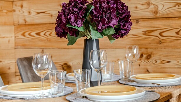 Un tavolo da pranzo in legno apparecchiato con piatti, bicchieri e un vaso di fiori viola.