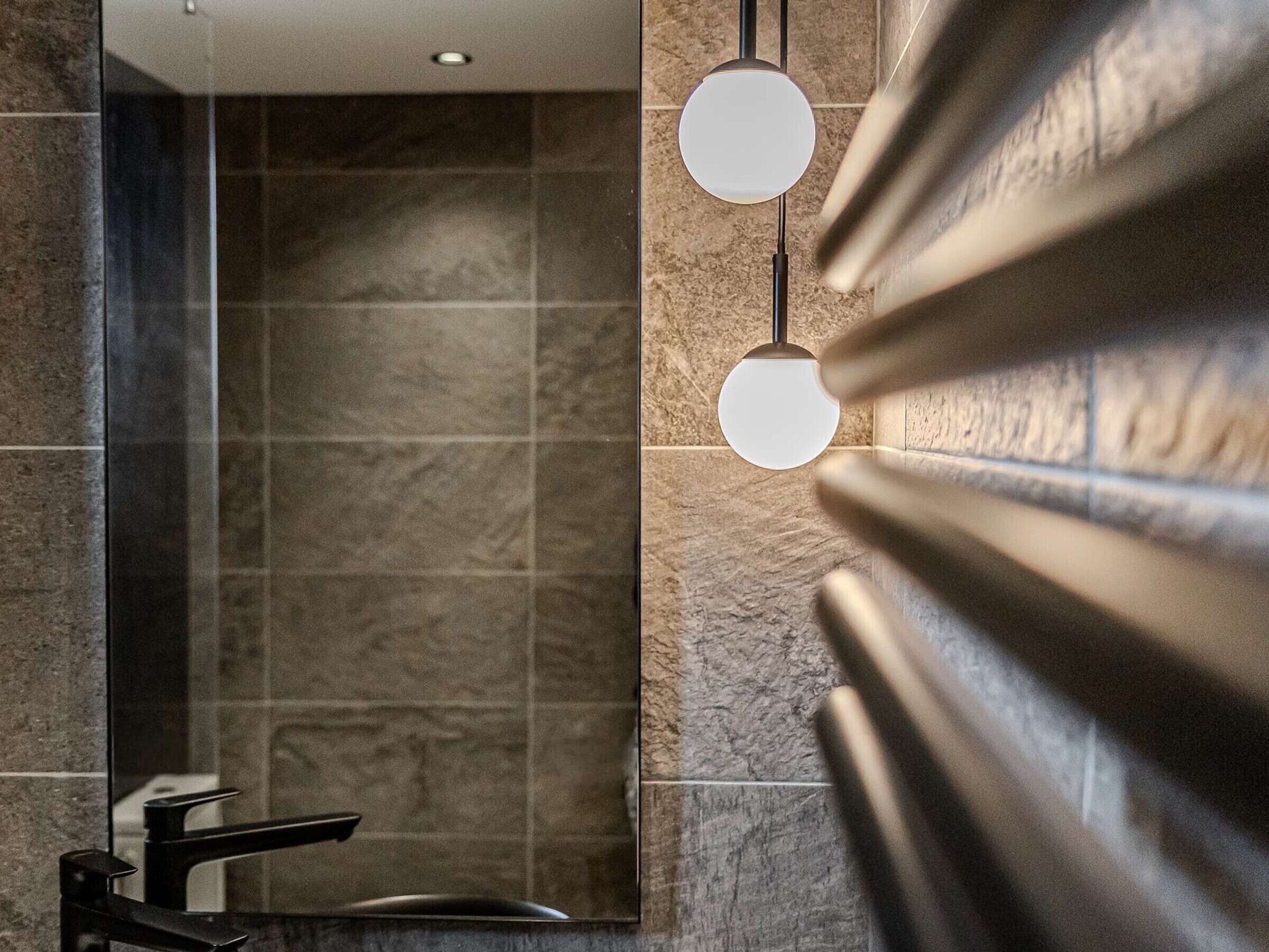 Um banheiro com design moderno, com área de chuveiro com porta de vidro, pia com torneira preta e duas luminárias pendentes.