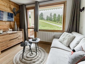 Ein gemütliches Wohnzimmer mit einer Couch, einem kleinen Tisch und Blick auf eine grüne Landschaft durch ein großes Fenster.