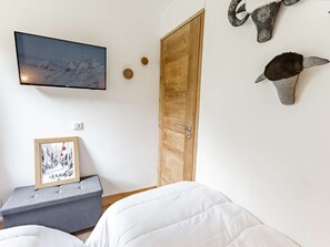A room with a bed, a television mounted on the wall, a wooden door, and wall-mounted animal horns.