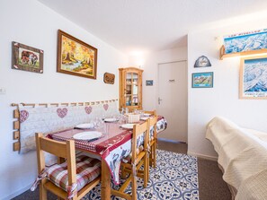 A dining area with a table set for four, wooden chairs, a cabinet, and wall art. - Spacious apartment, slopes view - 7 guests (Le Corbier)