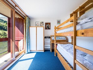 Quarto com beliches, guarda-roupa, escrivaninha com rádio e janela com cortinas.
