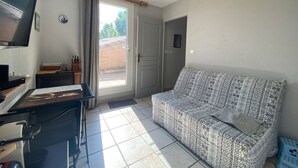 A living room with a sofa, a television, a desk with a computer, and a window with curtains. - Calm apartment near the beach - 2 guests (Bouzigues)