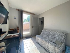 A living room with a sofa, a television, a desk with a computer, and a window with curtains. - Calm apartment near the beach - 2 guests (Bouzigues)