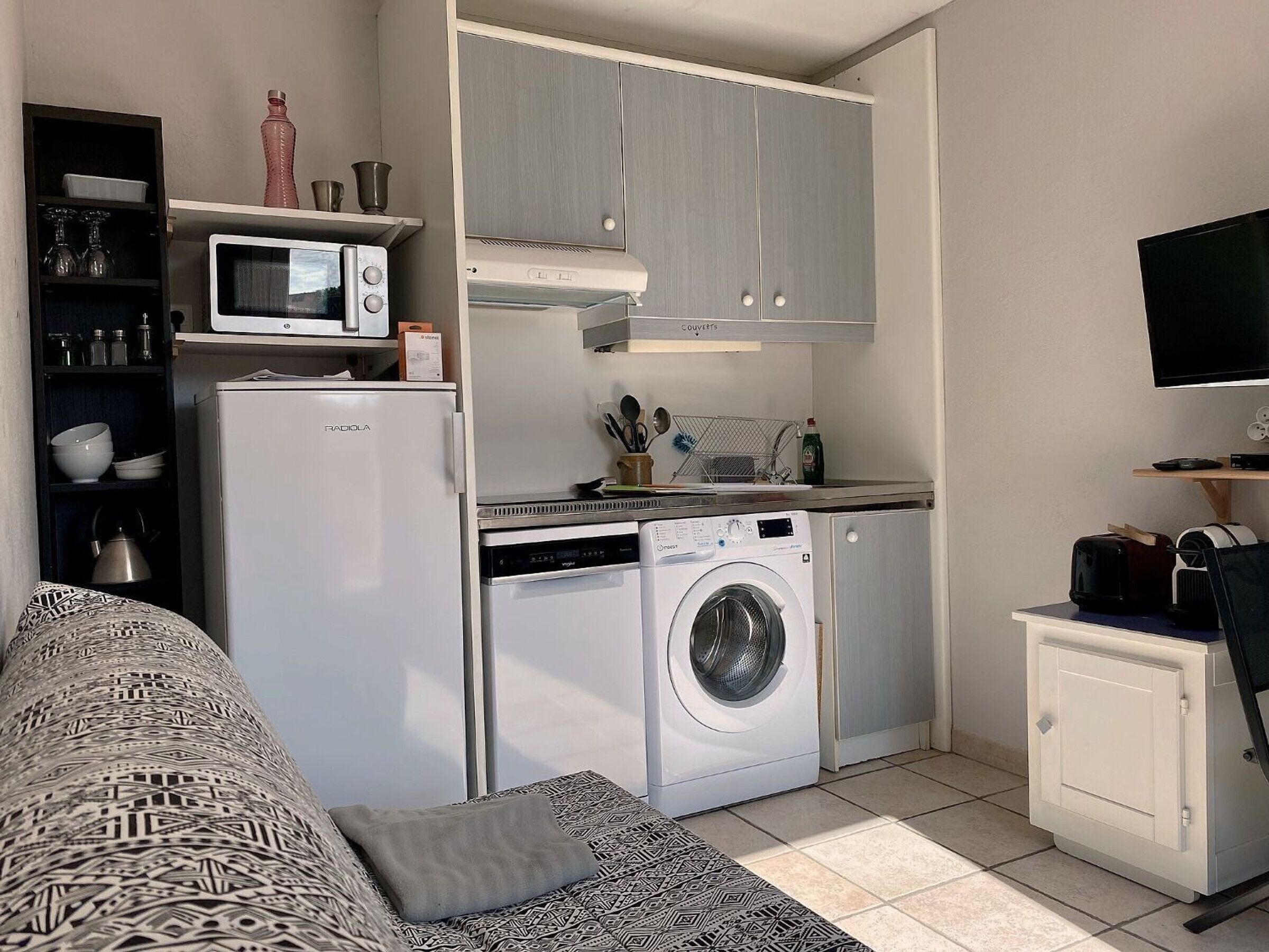 Eine kleine Küchenzeile mit Mikrowelle, Kühlschrank, Waschmaschine und einem Hängeschrank.