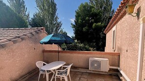 A patio with a table and chairs, an air conditioning unit, and a blue umbrella. - Calm apartment near the beach - 2 guests (Bouzigues)